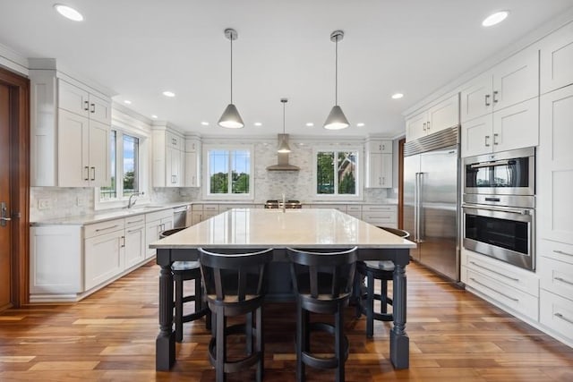 kitchen with white cabinetry, a kitchen island, stainless steel appliances, and wall chimney range hood