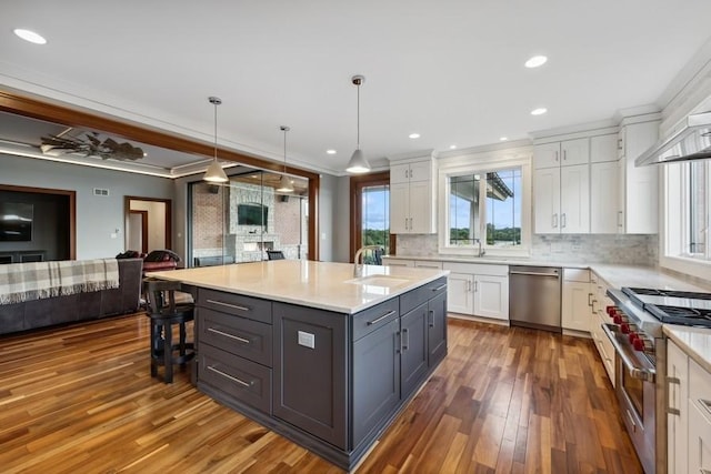 kitchen featuring appliances with stainless steel finishes, tasteful backsplash, a center island with sink, white cabinets, and hanging light fixtures