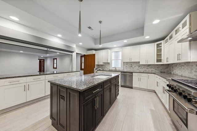 kitchen with dark brown cabinetry, sink, stainless steel appliances, dark stone counters, and a kitchen island with sink