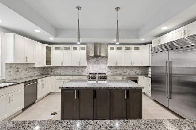 kitchen with light stone countertops, a center island with sink, wall chimney exhaust hood, and appliances with stainless steel finishes