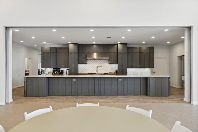 kitchen featuring sink, wall chimney range hood, backsplash, a large island with sink, and gray cabinets