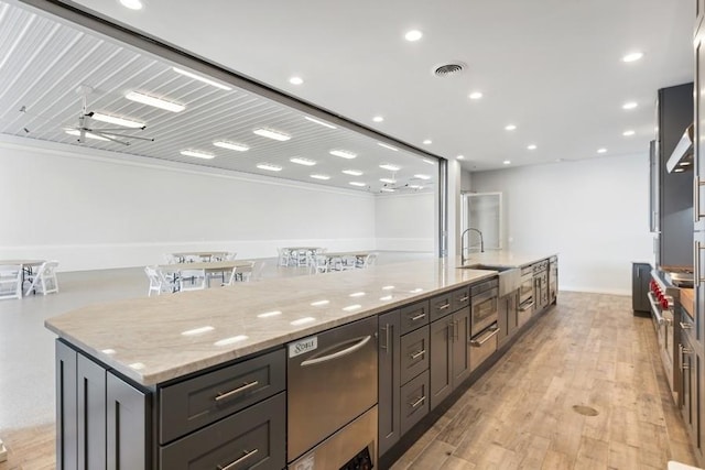 kitchen featuring light stone countertops, sink, ceiling fan, a large island, and light hardwood / wood-style floors