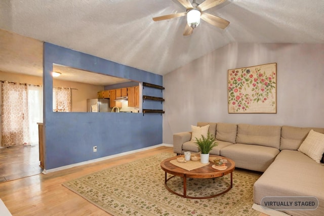 living room featuring a textured ceiling, light wood-type flooring, ceiling fan, and lofted ceiling