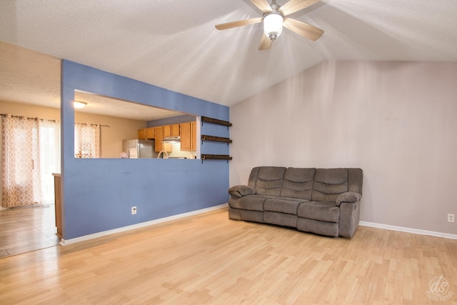 living room featuring a textured ceiling, light wood-type flooring, vaulted ceiling, and ceiling fan