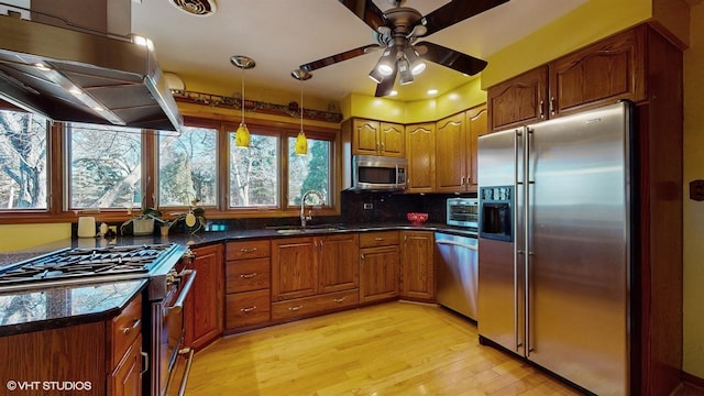 kitchen with island range hood, stainless steel appliances, a sink, brown cabinets, and dark countertops