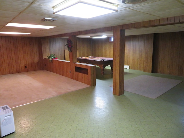 basement with a paneled ceiling, wooden walls, and pool table