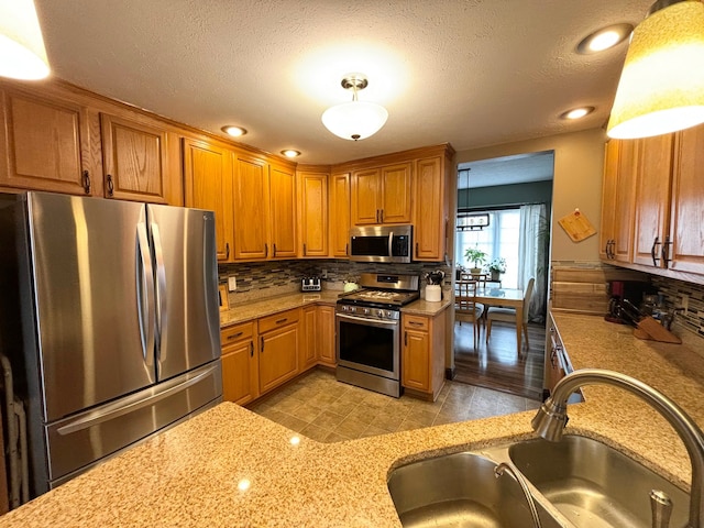 kitchen featuring stainless steel appliances, backsplash, sink, light stone counters, and a textured ceiling