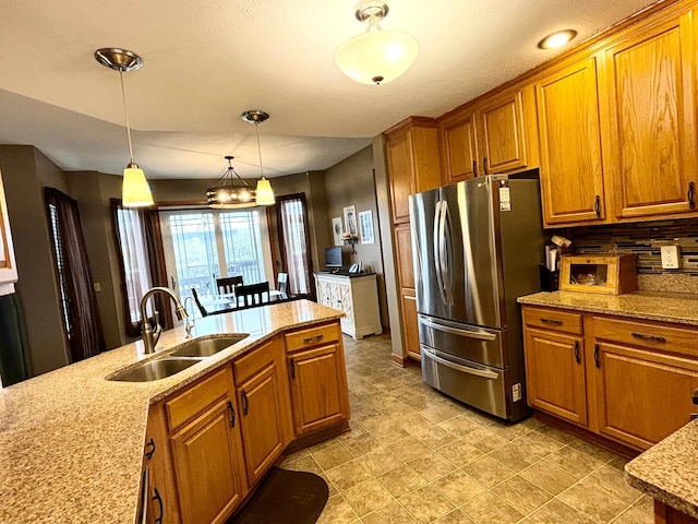 kitchen featuring tasteful backsplash, stainless steel refrigerator, sink, pendant lighting, and light stone counters