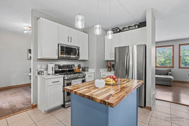 kitchen featuring appliances with stainless steel finishes, light wood-type flooring, decorative light fixtures, white cabinets, and a kitchen island