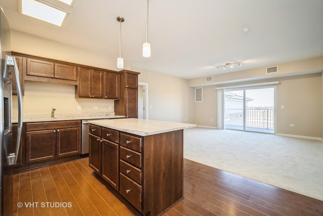 kitchen with dark carpet, hanging light fixtures, a center island, light stone countertops, and stainless steel fridge with ice dispenser