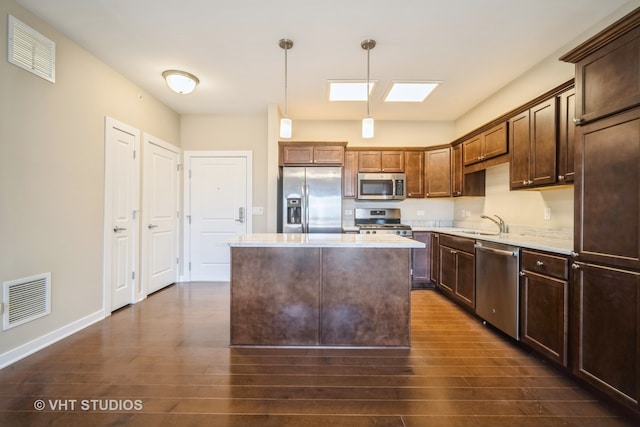 kitchen with appliances with stainless steel finishes, sink, a kitchen island, dark hardwood / wood-style flooring, and decorative light fixtures