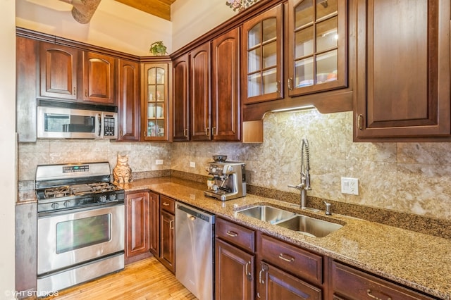 kitchen featuring decorative backsplash, appliances with stainless steel finishes, light stone countertops, light wood-type flooring, and sink