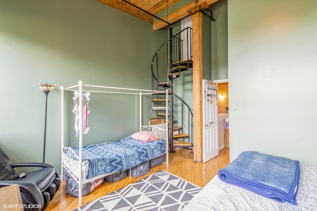 bedroom featuring beamed ceiling, a high ceiling, wood ceiling, and wood-type flooring