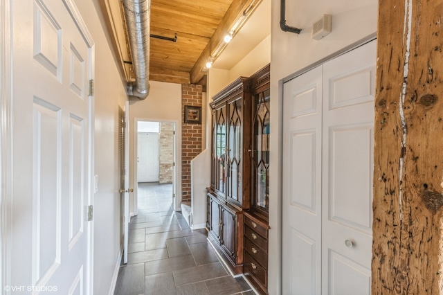 hallway with dark tile patterned flooring, wood ceiling, and brick wall