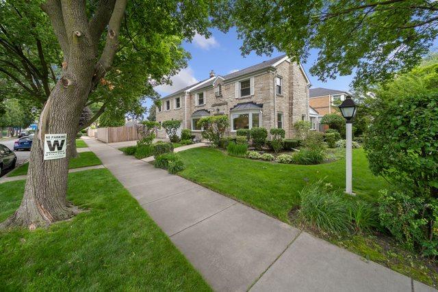 traditional-style house with a front lawn, fence, and stone siding