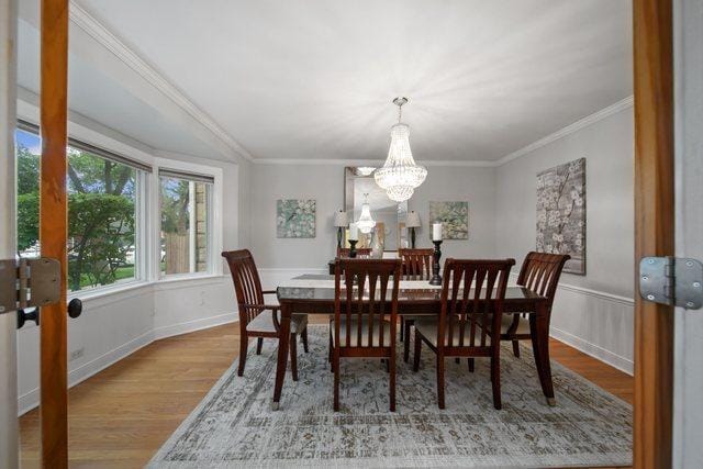 dining room with crown molding, baseboards, a wainscoted wall, wood finished floors, and a notable chandelier