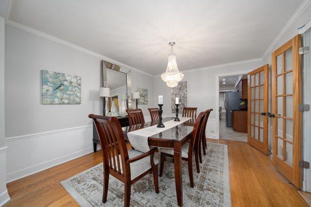 dining space featuring french doors, light wood-style floors, wainscoting, crown molding, and a chandelier