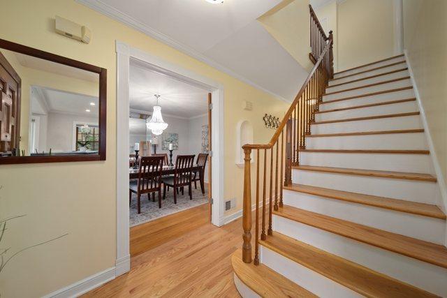 staircase with an inviting chandelier, wood finished floors, baseboards, and ornamental molding