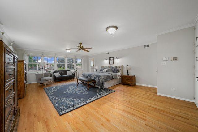 bedroom with a ceiling fan, visible vents, baseboards, ornamental molding, and light wood-style floors