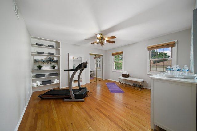 exercise room featuring visible vents, built in shelves, baseboards, light wood-style floors, and a ceiling fan