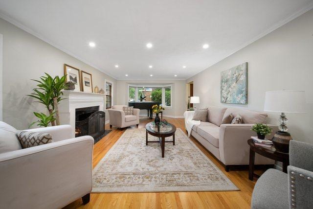 living area with crown molding, recessed lighting, light wood-type flooring, and a warm lit fireplace