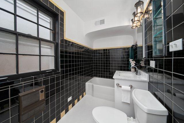 full bath featuring visible vents, toilet, a tub, heating unit, and tile walls