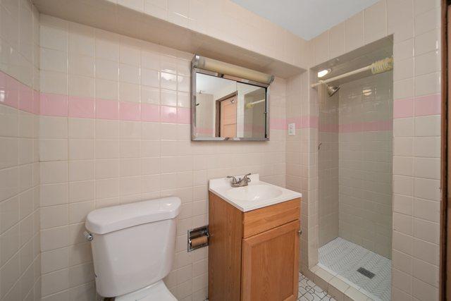 full bathroom with vanity, tile walls, toilet, and tiled shower