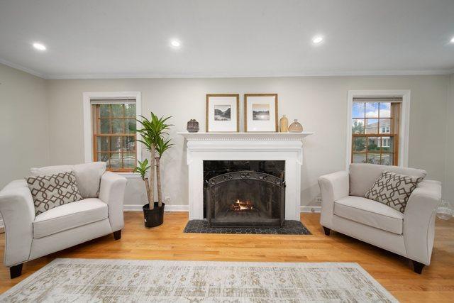 living area with crown molding, a fireplace with flush hearth, wood finished floors, and baseboards