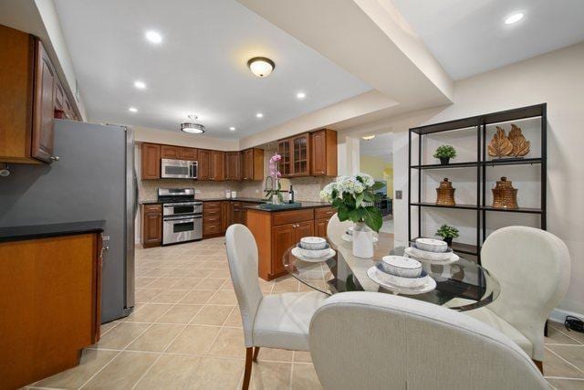 kitchen featuring brown cabinets, glass insert cabinets, appliances with stainless steel finishes, dark countertops, and tasteful backsplash