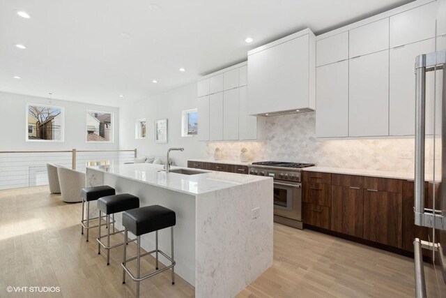 kitchen featuring sink, high end range, dark brown cabinetry, a center island with sink, and light wood-type flooring