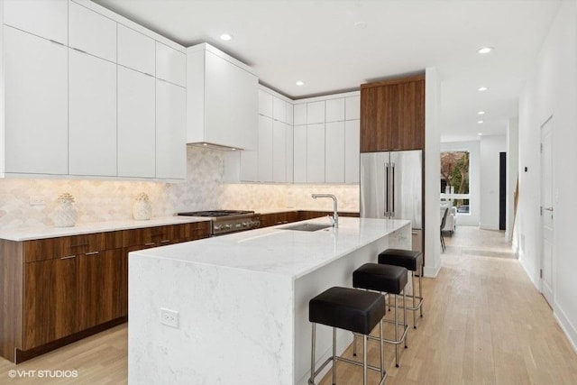 kitchen featuring high quality fridge, white cabinetry, sink, a breakfast bar area, and a kitchen island with sink