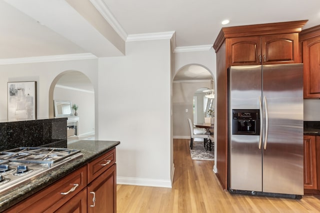 kitchen with crown molding, stainless steel appliances, light wood-type flooring, and dark stone countertops