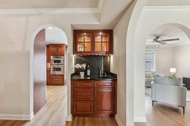 bar featuring double oven, backsplash, dark stone counters, crown molding, and light hardwood / wood-style floors