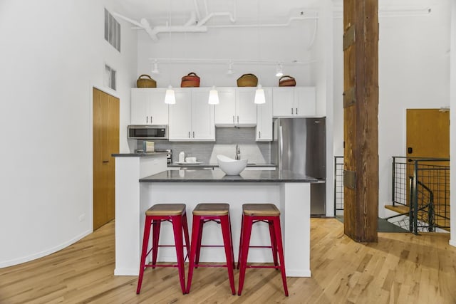 kitchen featuring a center island, white cabinets, appliances with stainless steel finishes, tasteful backsplash, and a kitchen bar