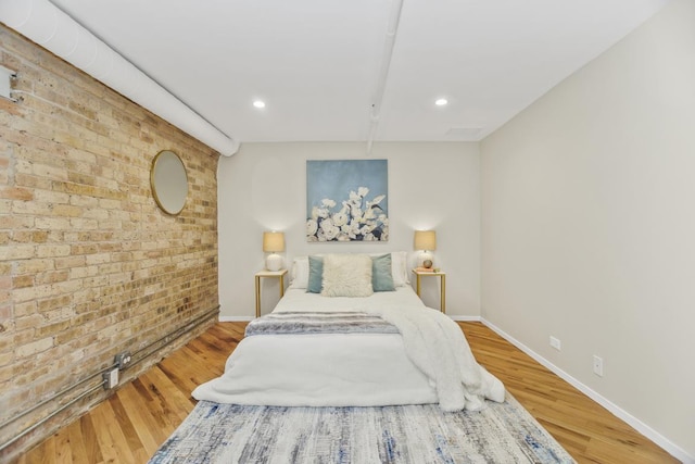 bedroom featuring hardwood / wood-style floors and brick wall