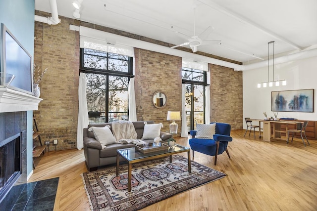 living room with ceiling fan, a high ceiling, brick wall, wood-type flooring, and a tiled fireplace