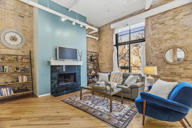 living room with a fireplace, wood-type flooring, a towering ceiling, and brick wall