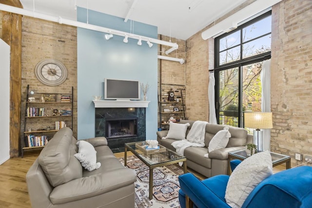 living room with hardwood / wood-style floors, brick wall, a towering ceiling, and a high end fireplace