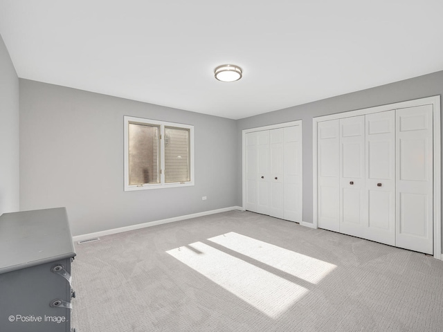 unfurnished bedroom featuring light carpet and two closets