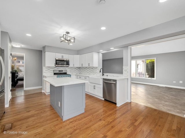 kitchen with tasteful backsplash, white cabinetry, light wood-type flooring, sink, and stainless steel appliances