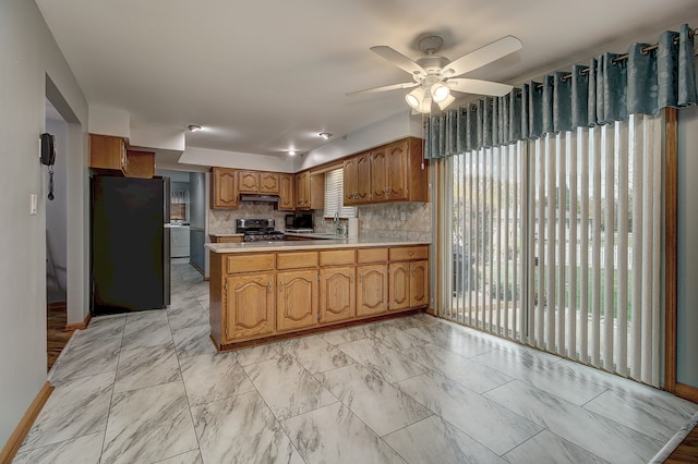 kitchen with backsplash, stainless steel range oven, kitchen peninsula, black fridge, and ceiling fan