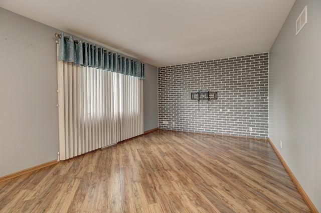 unfurnished room with brick wall and hardwood / wood-style flooring