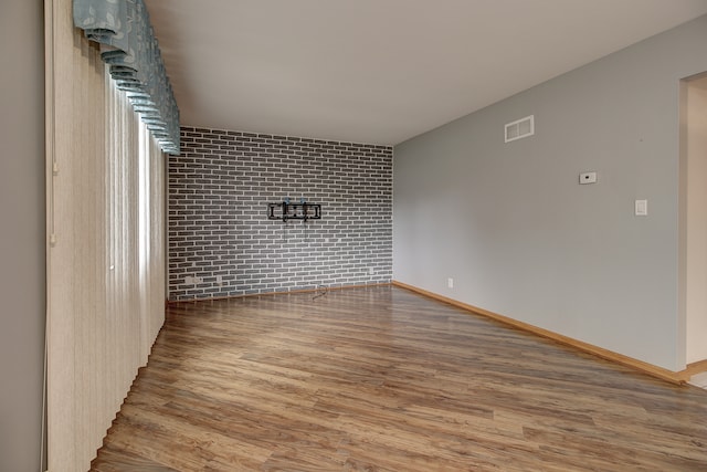 unfurnished room featuring hardwood / wood-style flooring and brick wall