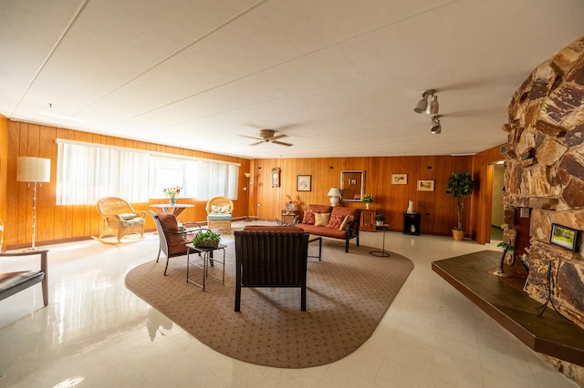 living room featuring ceiling fan, a stone fireplace, and wooden walls