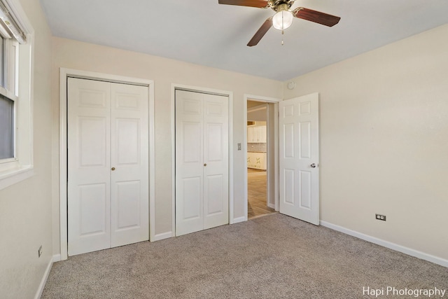 unfurnished bedroom featuring multiple closets, carpet flooring, and ceiling fan