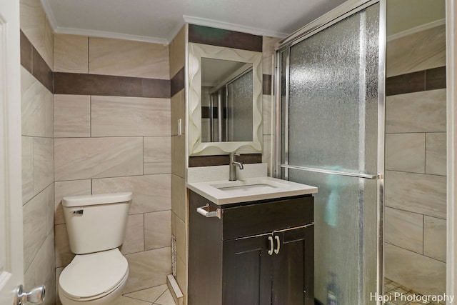 bathroom with toilet, a shower with shower door, crown molding, tile walls, and vanity