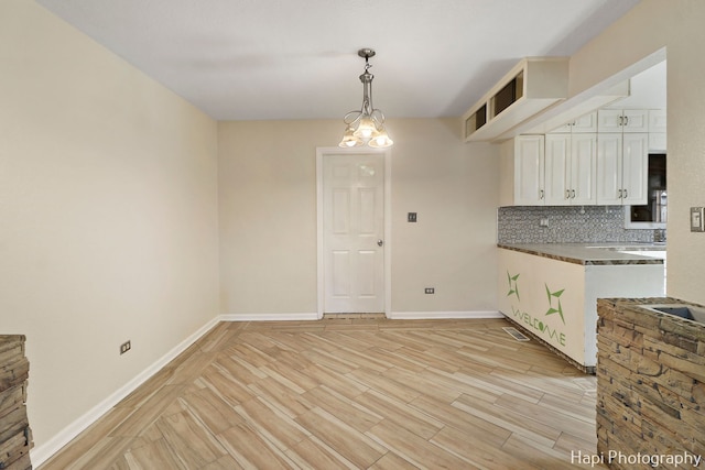 kitchen with tasteful backsplash, white cabinetry, light wood-type flooring, and decorative light fixtures