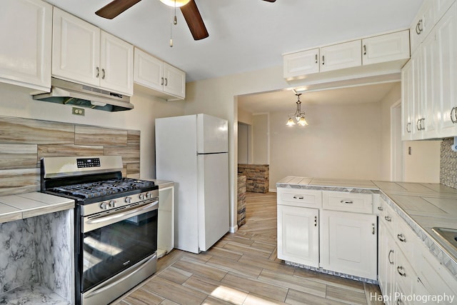 kitchen featuring pendant lighting, white refrigerator, gas stove, white cabinets, and tile countertops