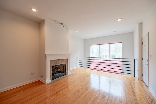 unfurnished living room featuring light hardwood / wood-style flooring, track lighting, and a tile fireplace