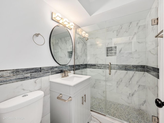 bathroom with vanity, a shower with shower door, tile walls, and toilet